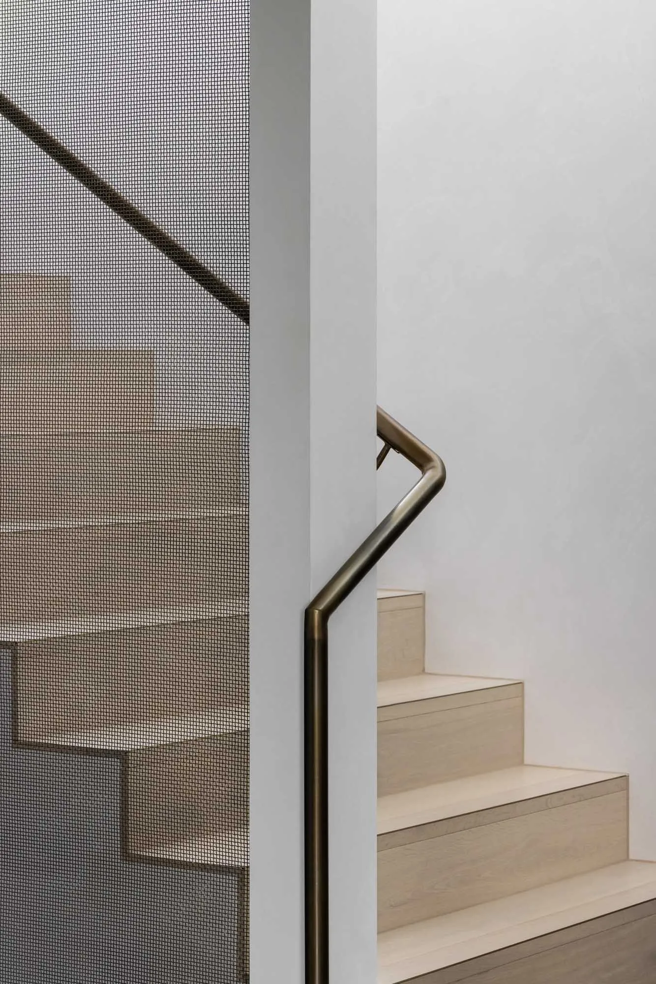 Modern wooden staircase with a bronze handrail and mesh guard.