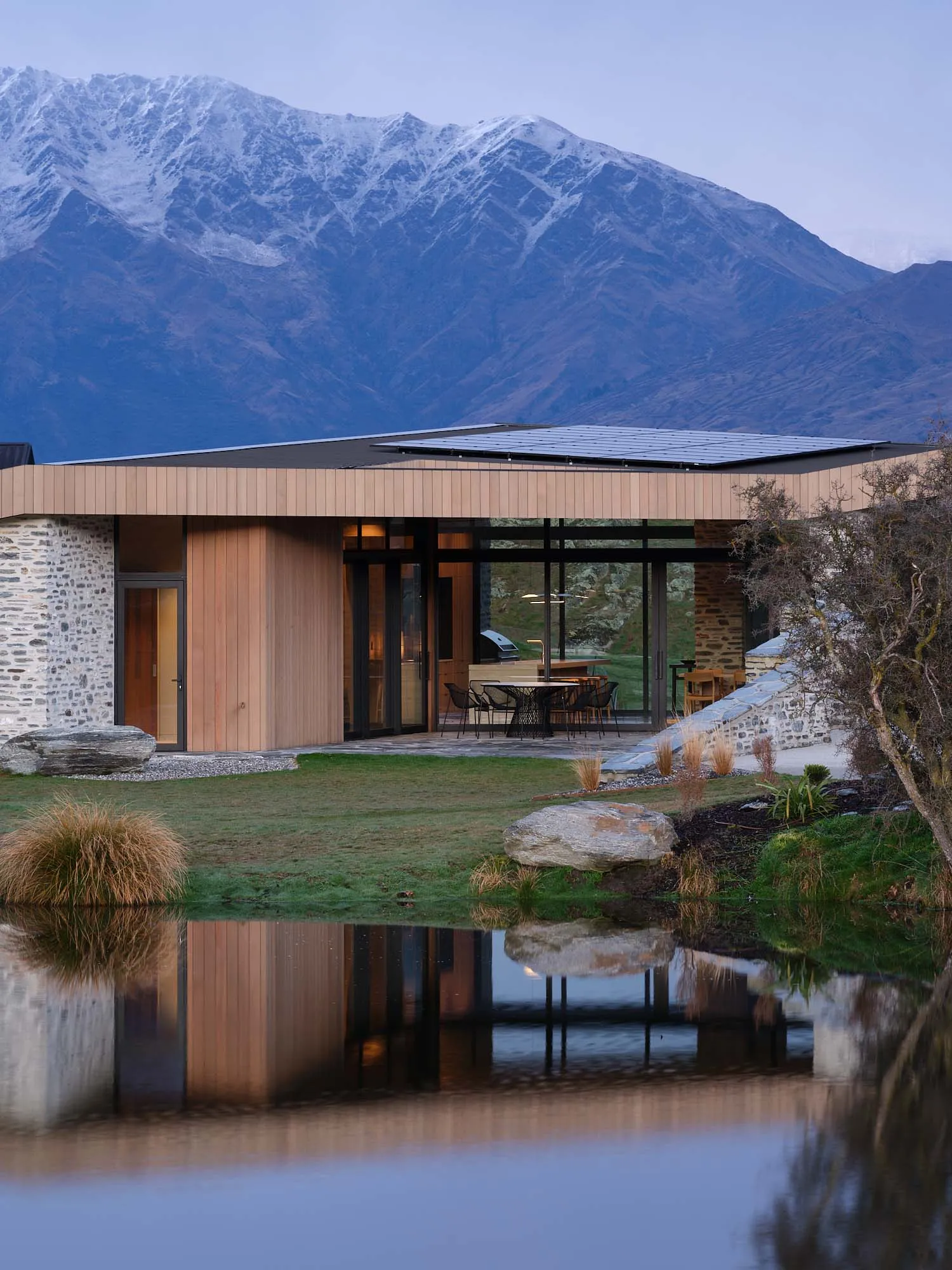 A modern house with wooden siding, concrete patio, and glass windows reflecting the natural surroundings.