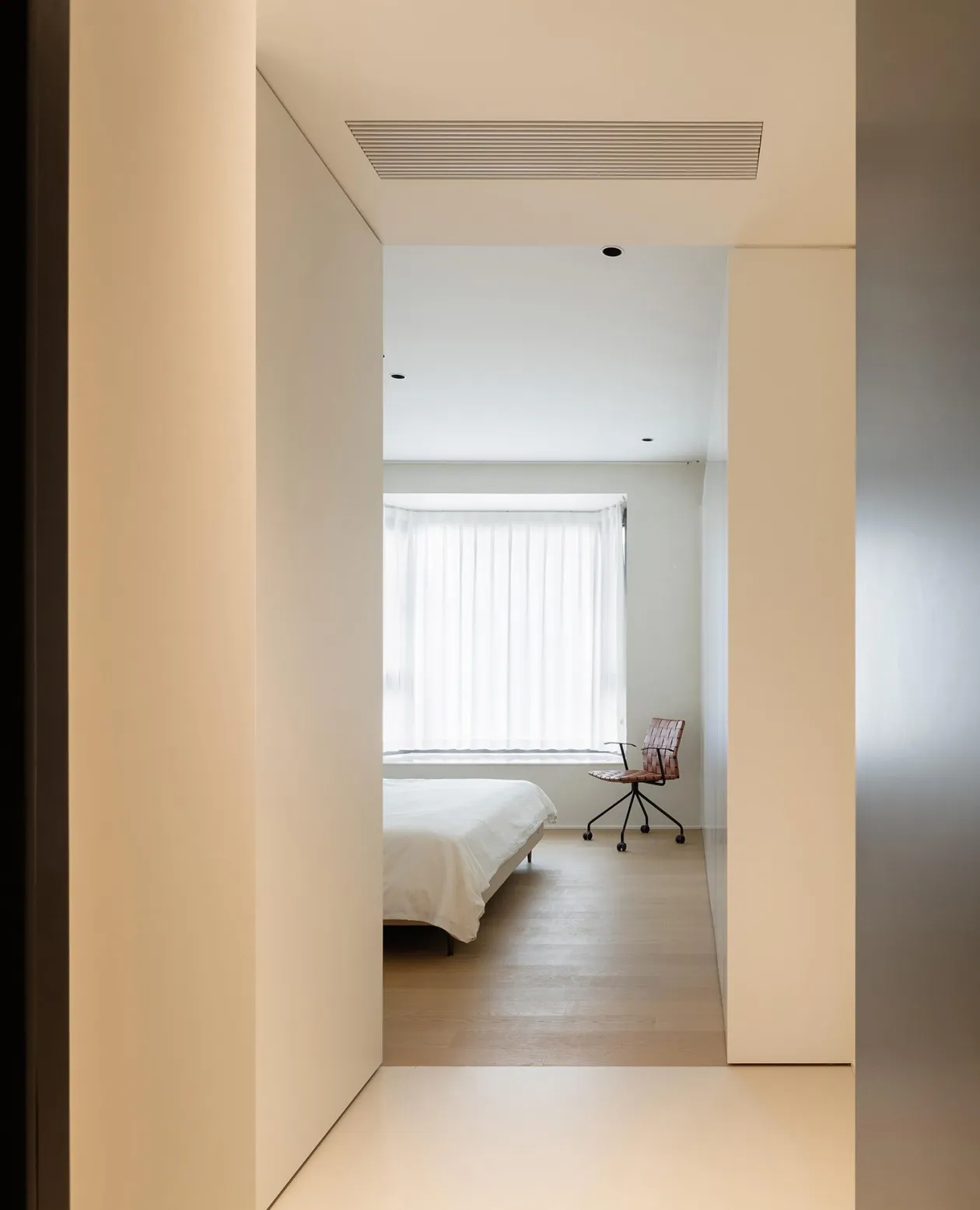 A minimalist bedroom with a white bed and a brown leather chair.
