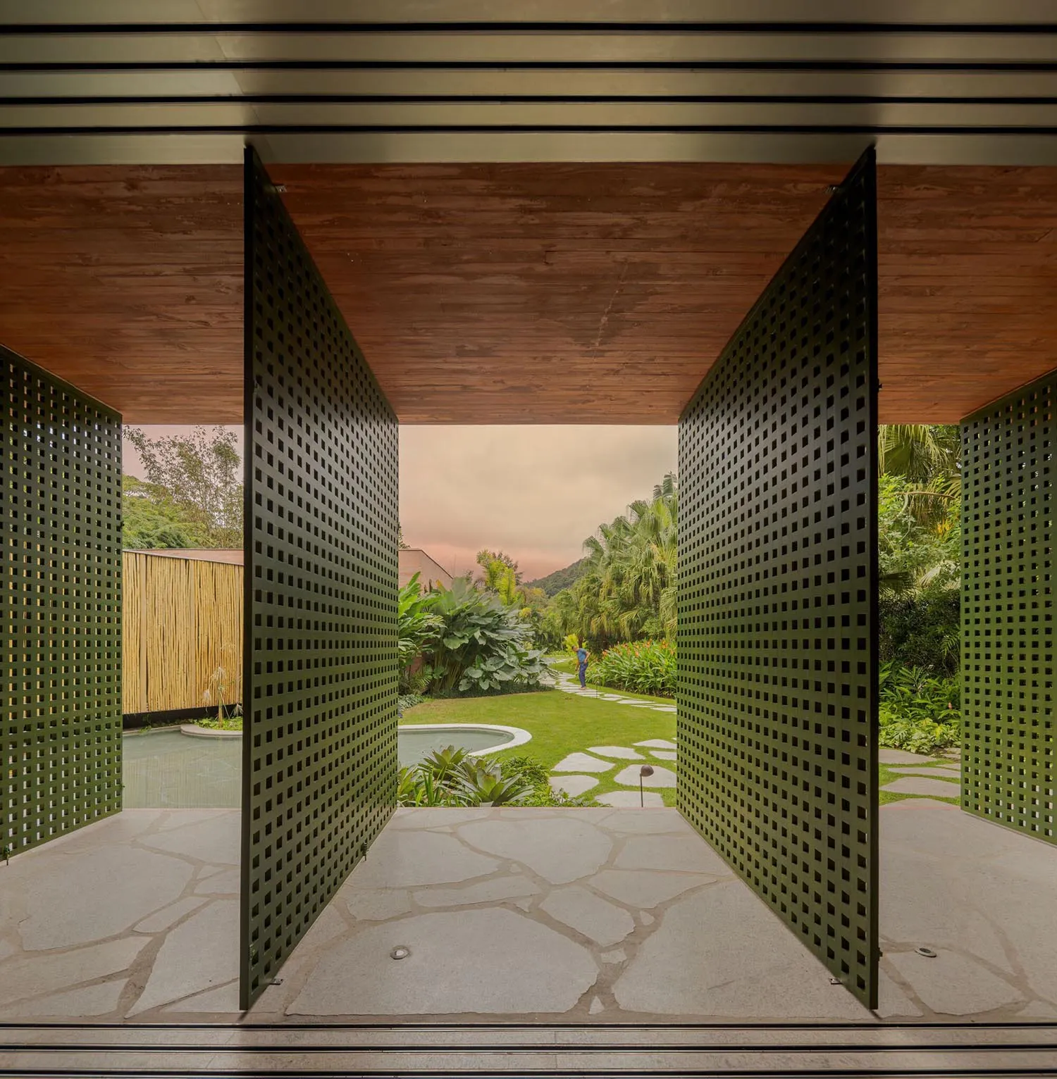Modern residential entryway featuring green metal perforated panels and natural stone flooring.