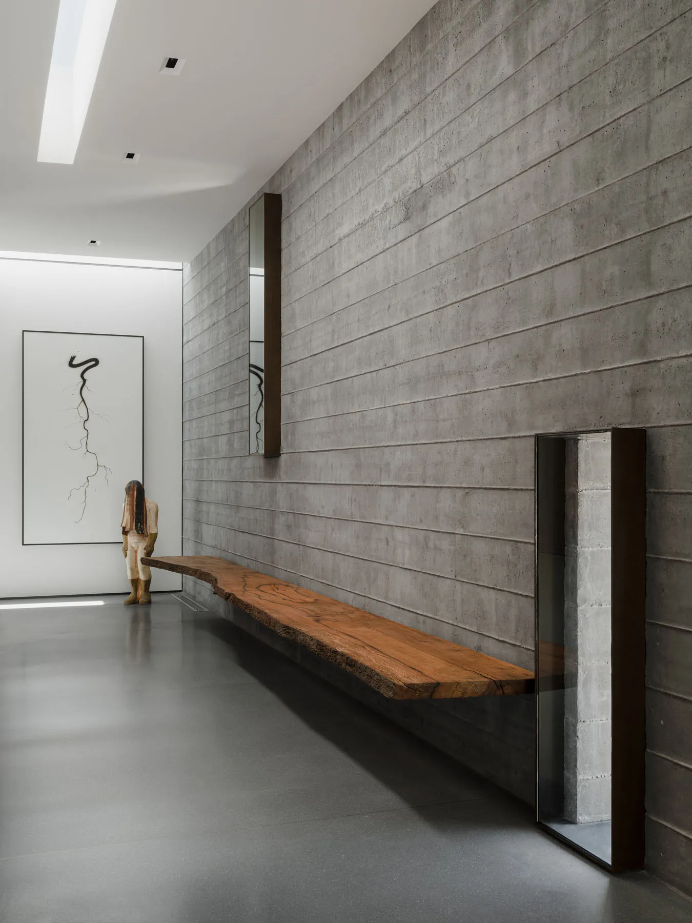 A sleek, modern lobby featuring a long, floating wooden bench against a textured concrete wall.