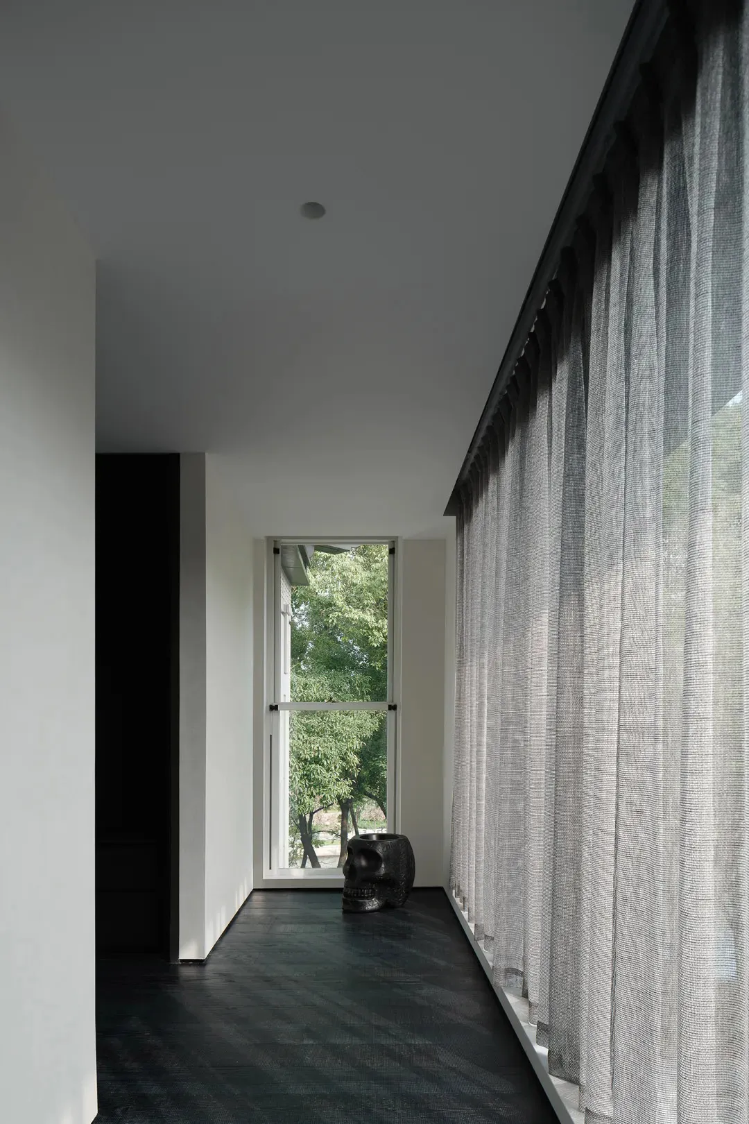 A minimalist bedroom featuring textured curtains and a dark floor, with a decorative skull on a table.