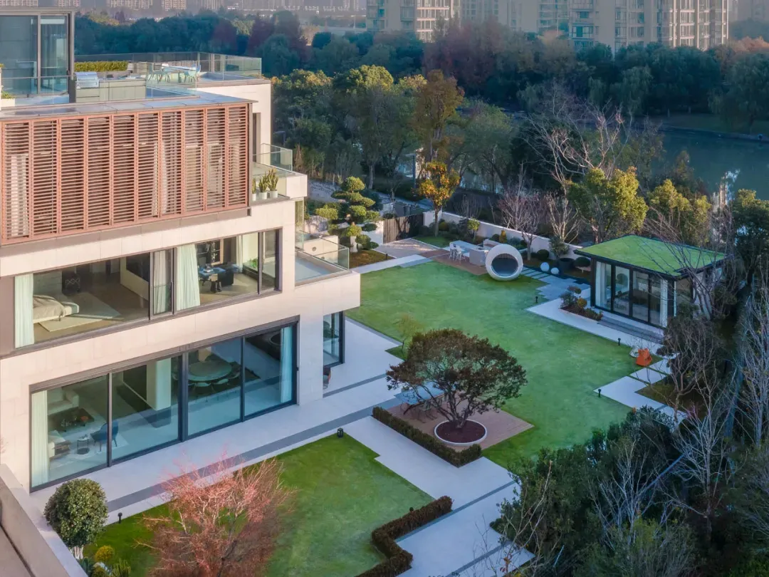 A modern house with a spacious outdoor garden featuring glass walls, concrete patio, and green lawn.