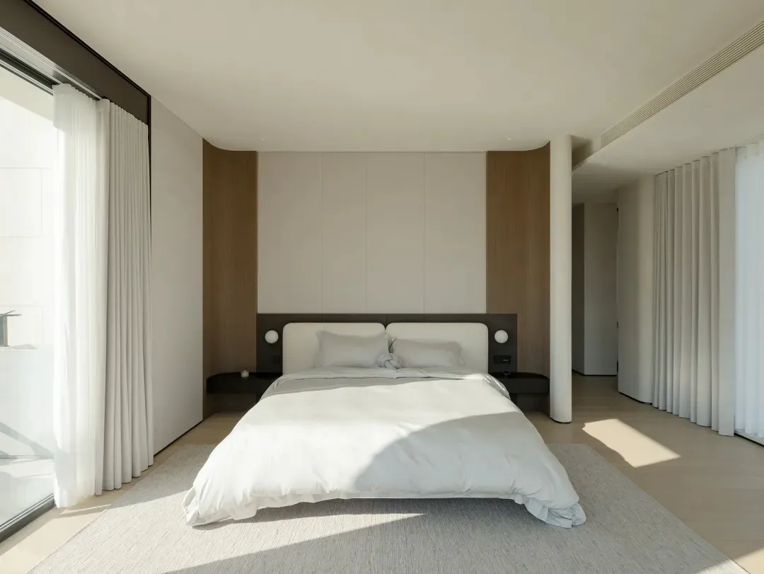Modern minimalist bedroom with white bedding, wooden accents, and large windows.