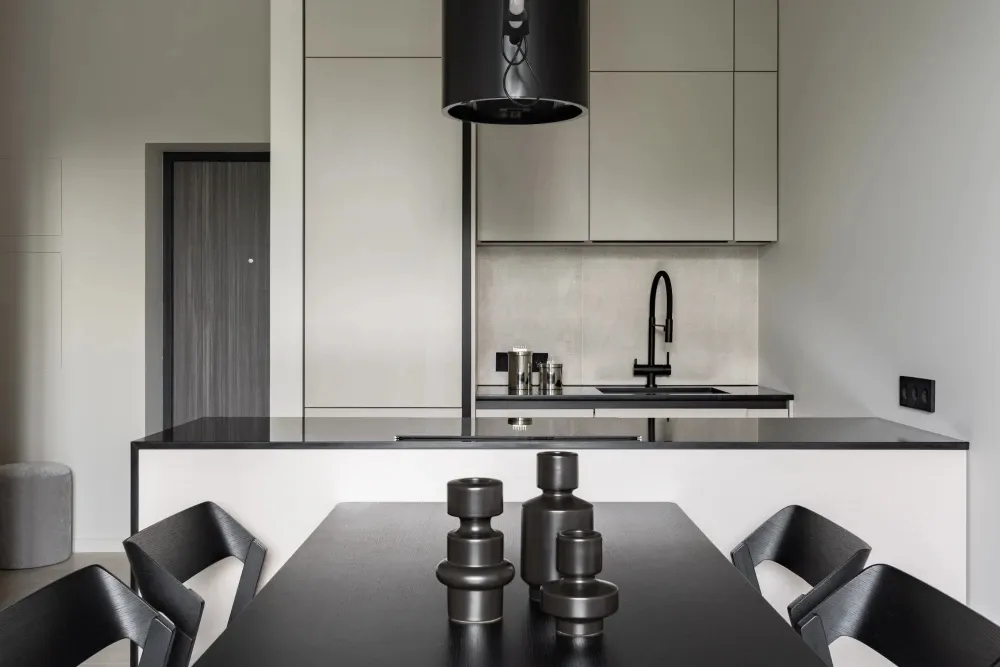 A modern, minimalist kitchen featuring black countertops, grey cabinets, and a glass backsplash.