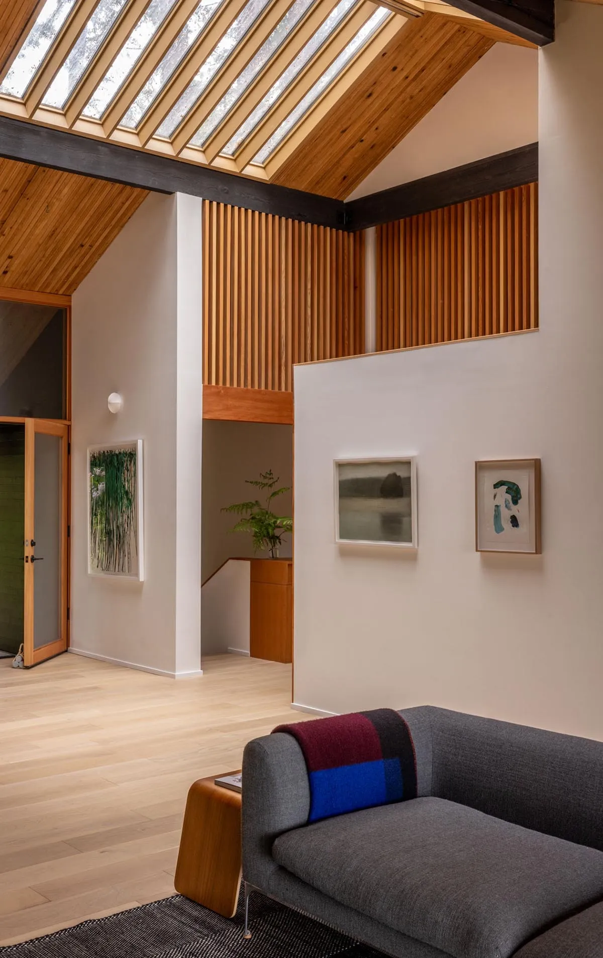 A contemporary living room featuring a wood-paneled wall and a gray sofa with a colorful throw blanket, under a slanted ceili