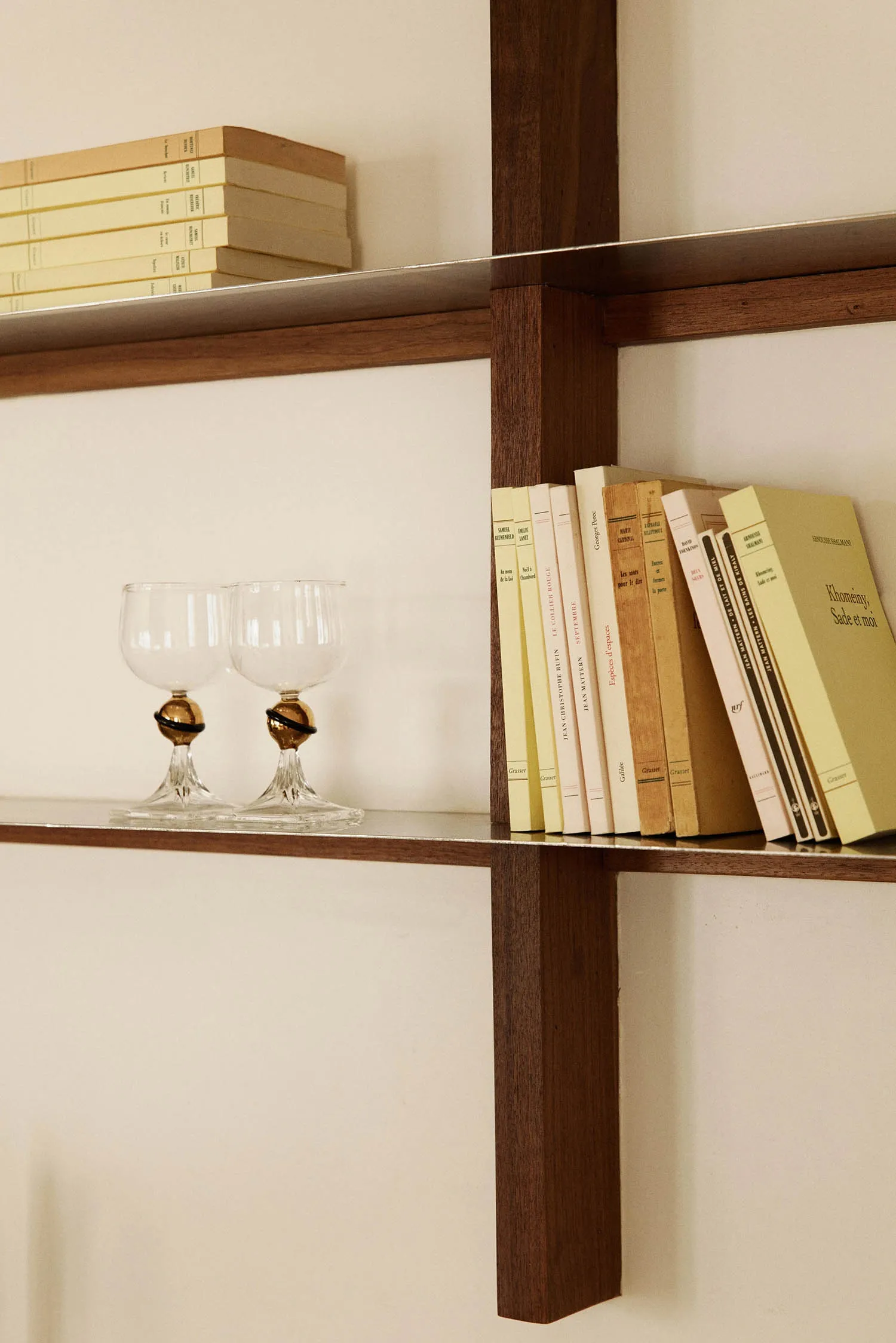 A modern bookshelf made of wood with books and wine glasses.