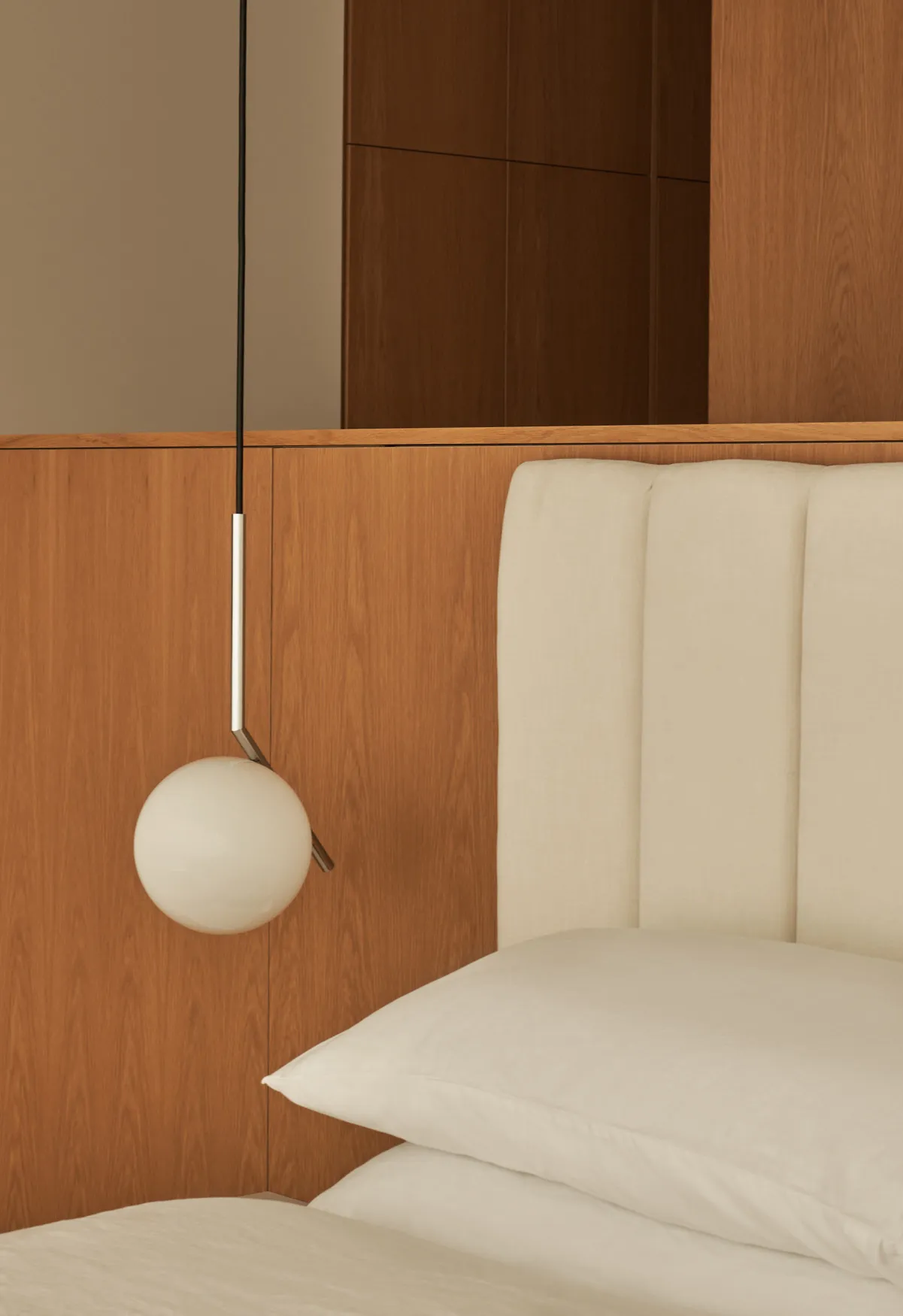 A modern minimalist bedroom featuring a wooden wardrobe and upholstered headboard with plush pillows.
