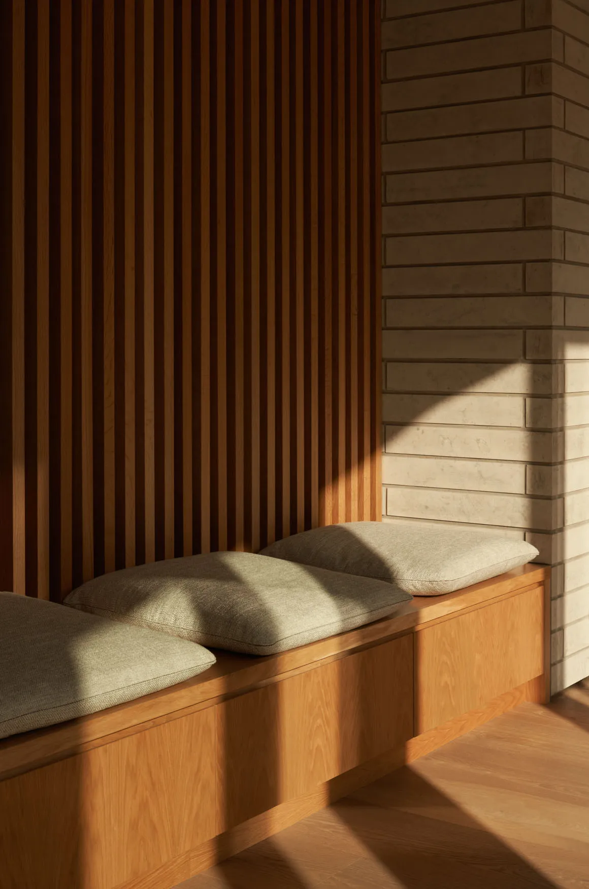 Modern window seat with wooden slatted wall and brick column, featuring cozy cushions.