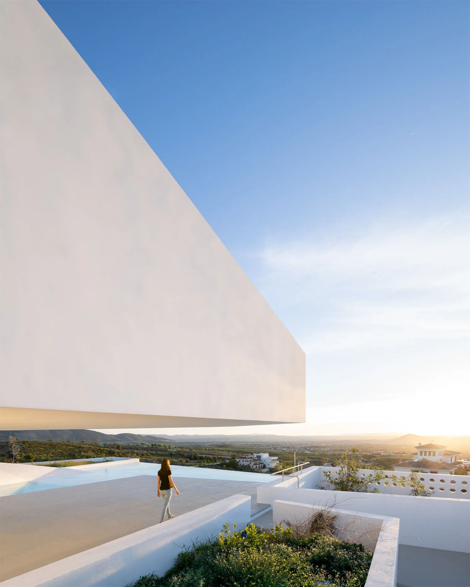 A modern white-rendered concrete architectural structure with a panoramic pool view.