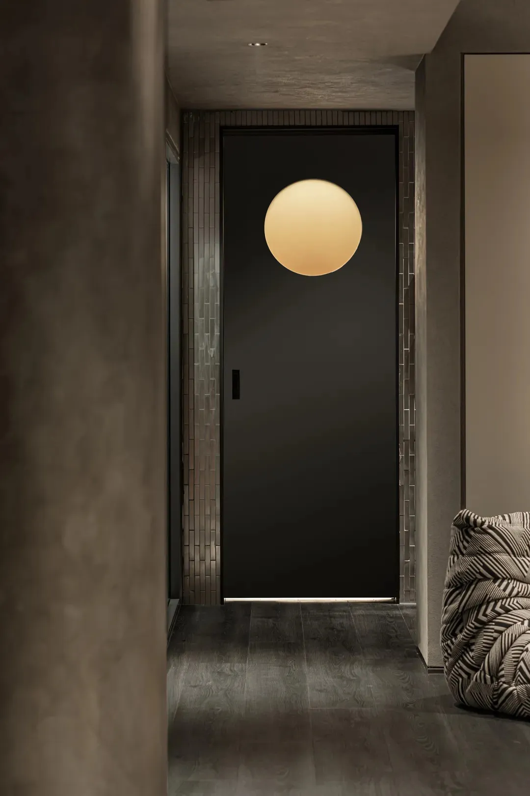 A minimalist design featuring a black door with metallic tiles on the sides and a circular light fixture.