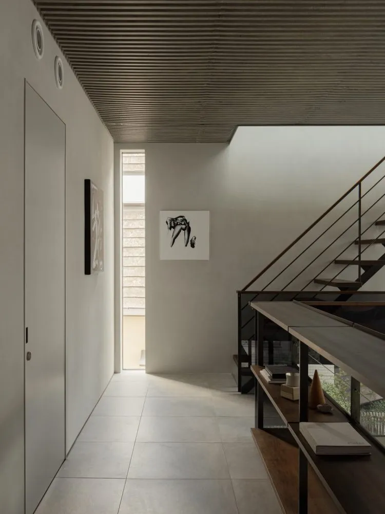 A modern minimalist hallway featuring concrete flooring, metal railings, and a concrete wall with a large window allowing nat