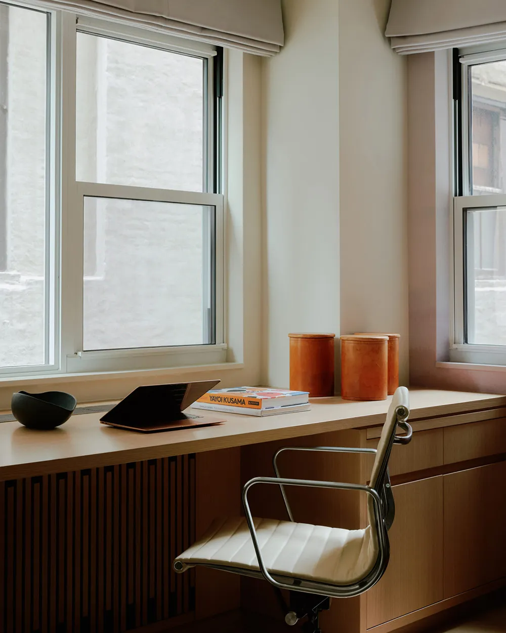 A minimalist industrial home office featuring a wooden desk with a leatherbound notebook, orange containers, and a white chai