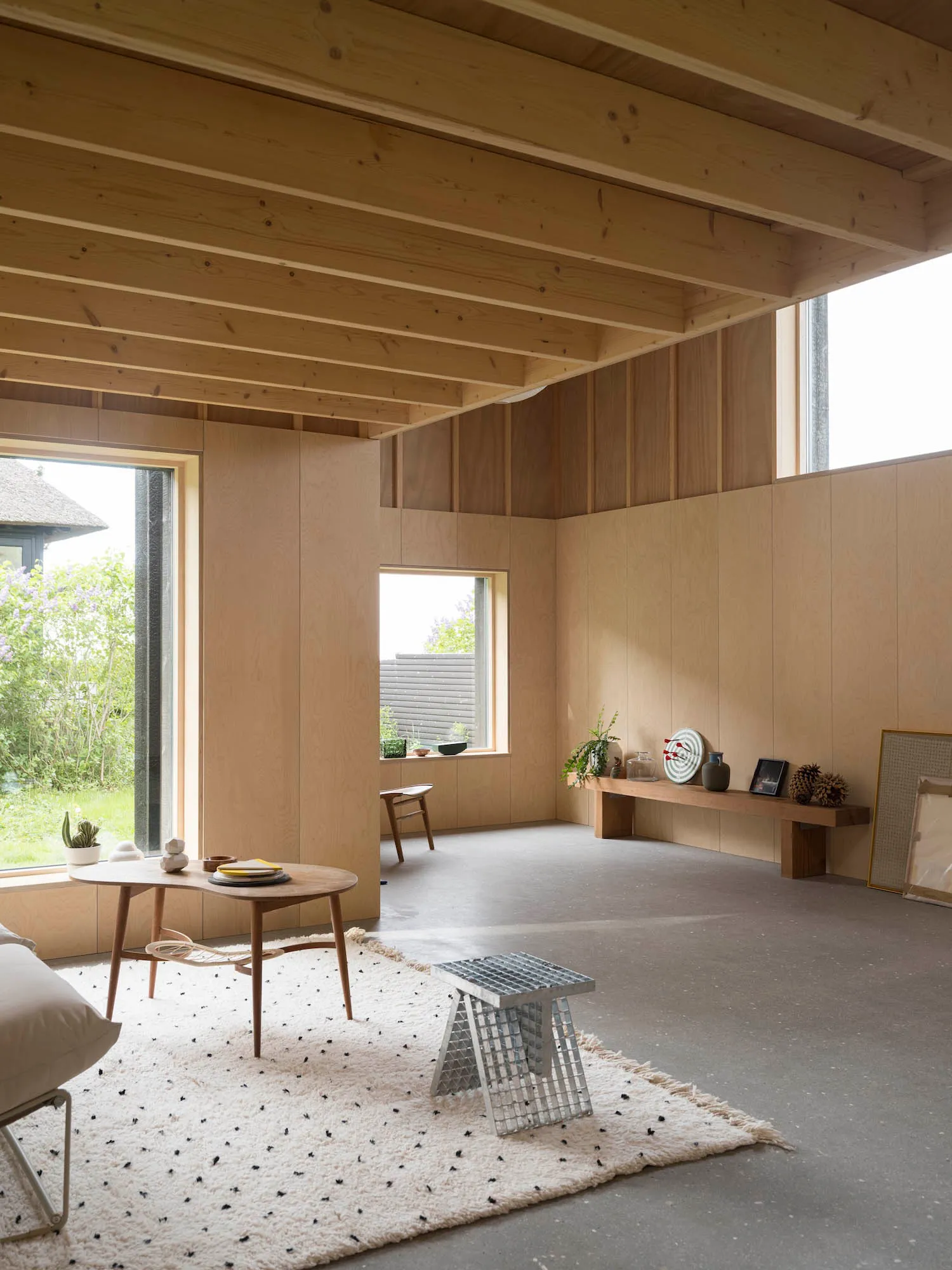 A minimalist living room with natural wood elements, featuring a coffee table, rug, and concrete floor.