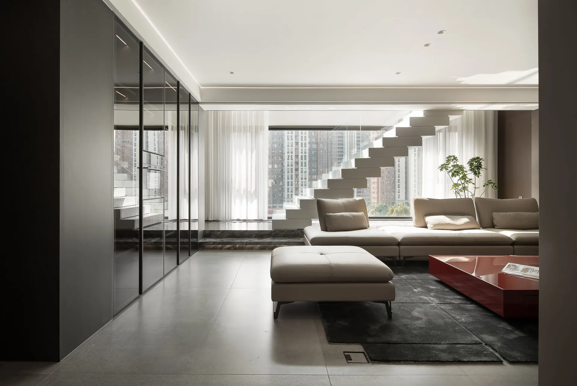 A modern living room featuring concrete walls and floors, with a large white couch and a red coffee table
