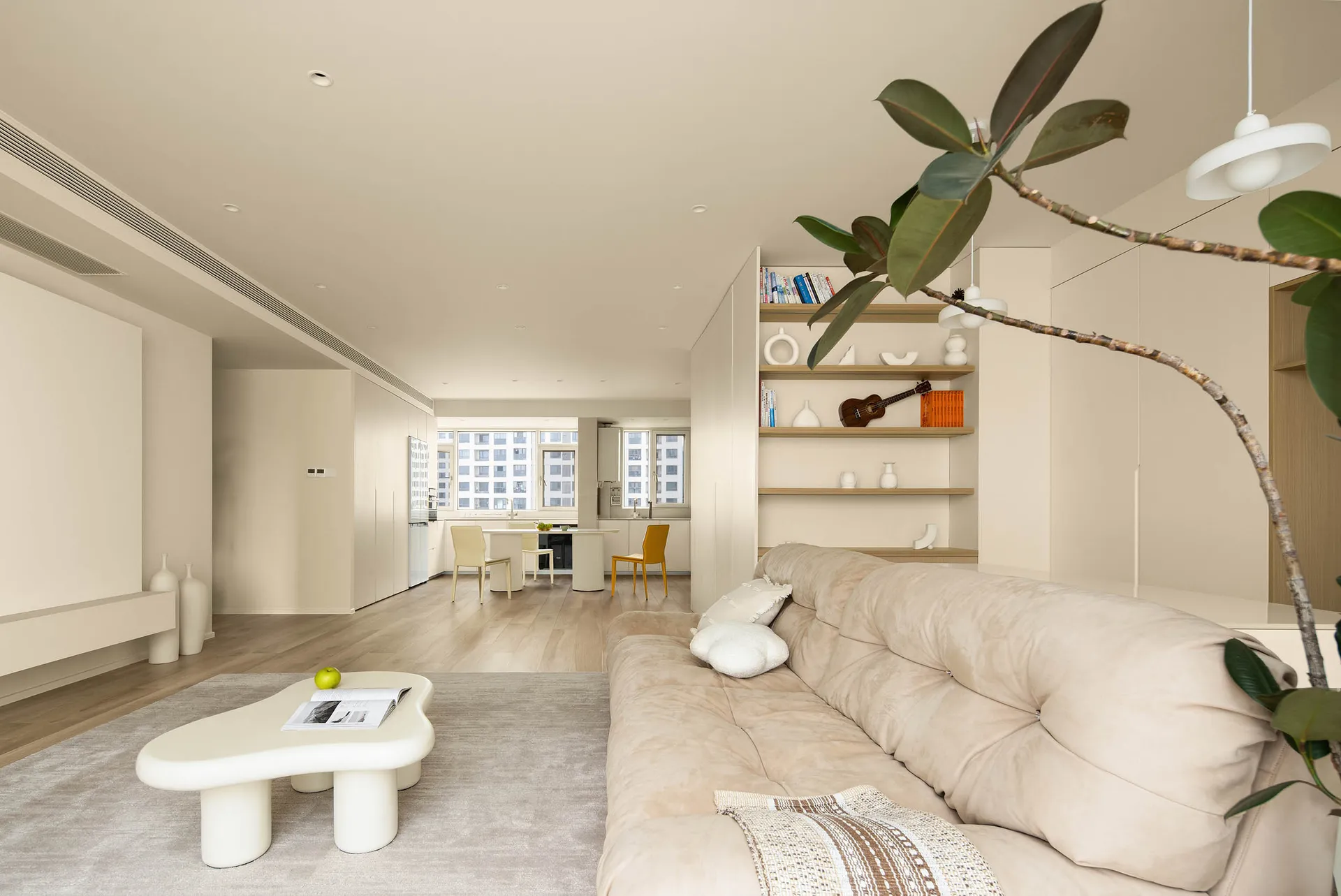 A minimalist living room with a beige couch, white coffee table, and a plant.