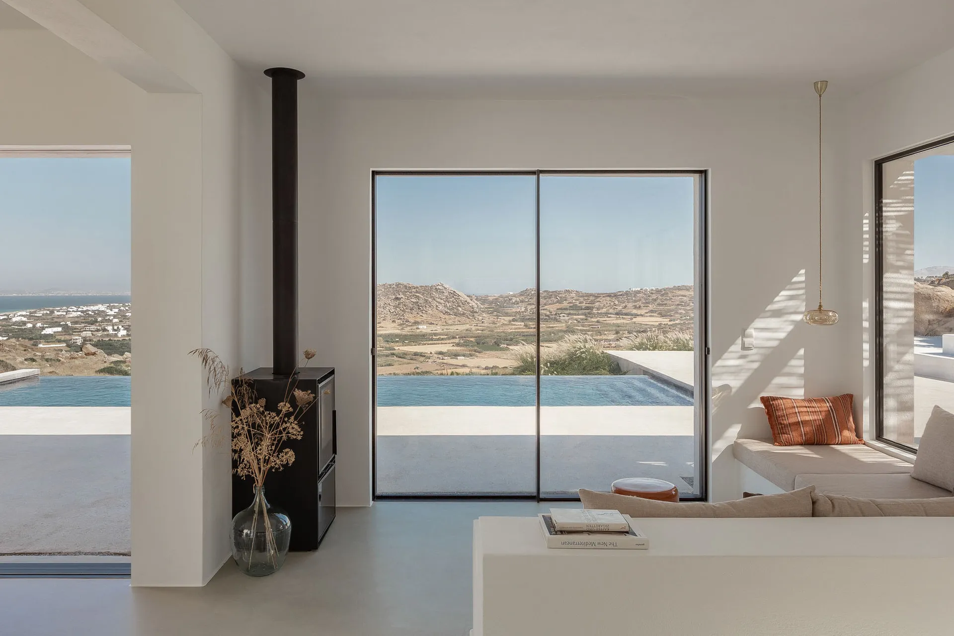 Modern minimalist living room with large windows overlooking the mountains and sea, featuring sleek concrete finishes and sim