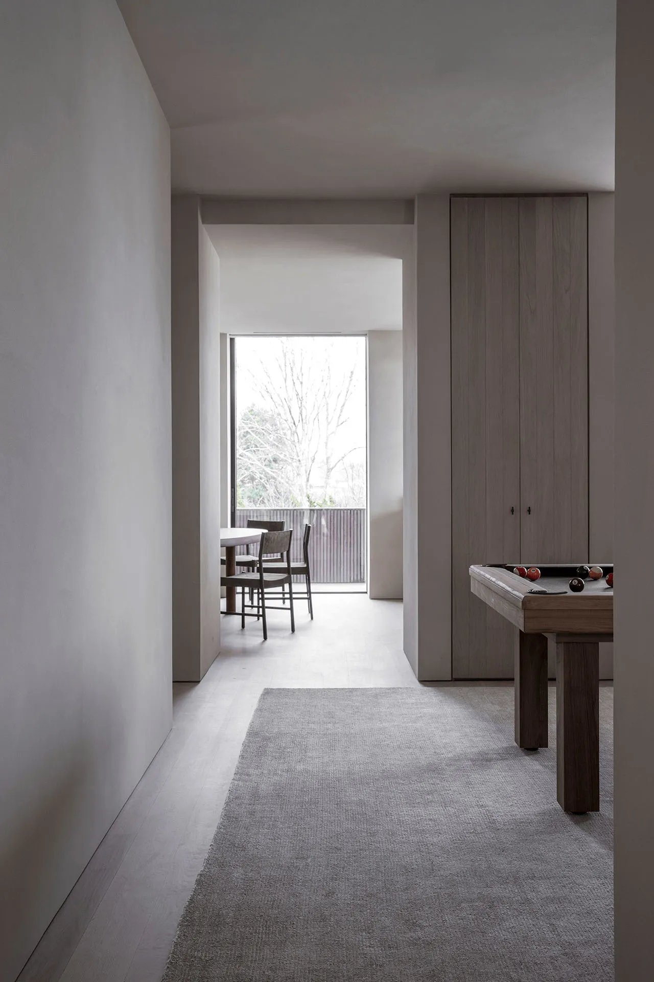 A modern minimalist living room featuring a wooden floor, minimalist furniture, and a large window with a view of trees.