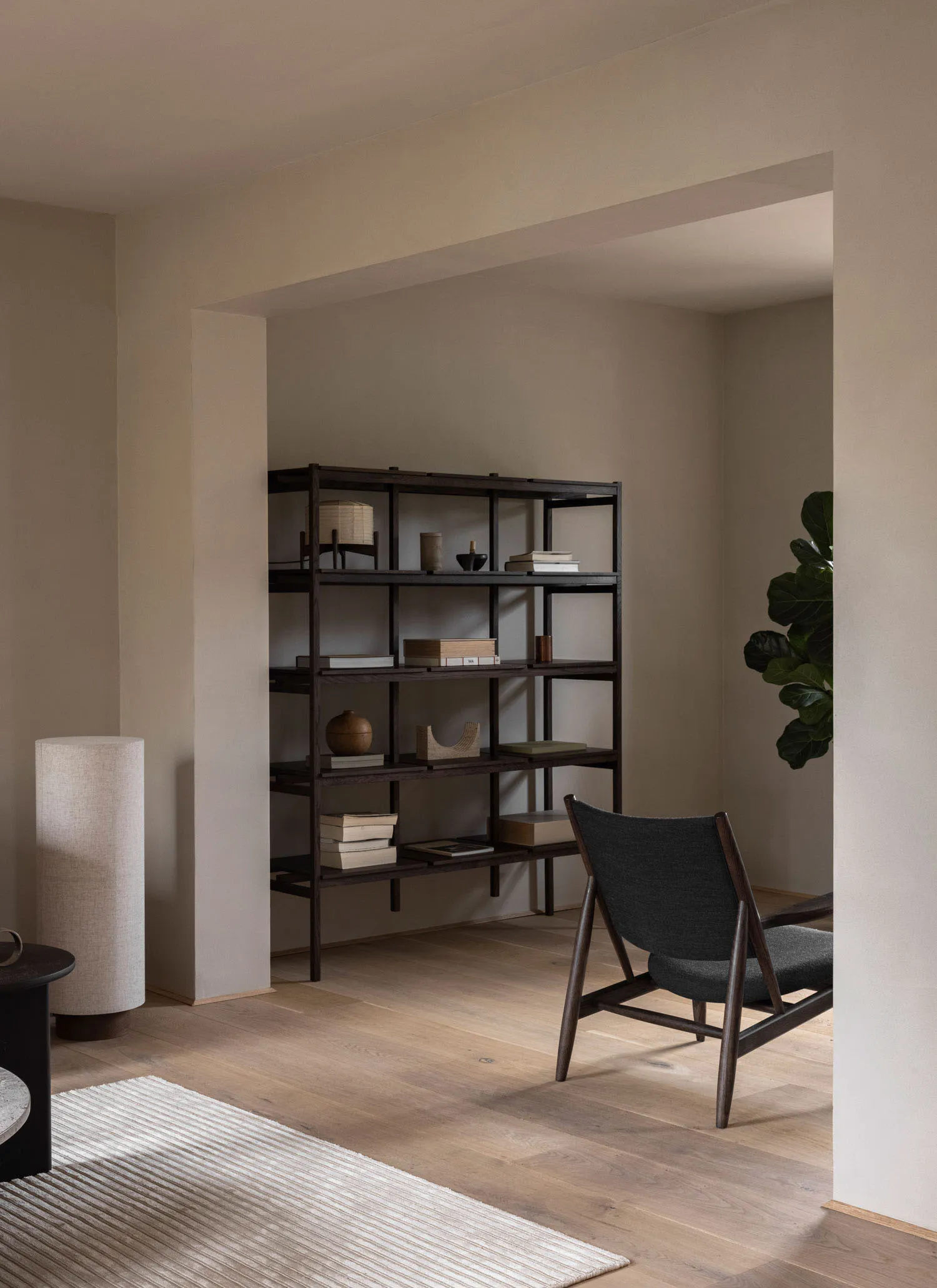 A minimalist living room featuring a wooden shelving unit with books, decorative objects, and a large chair with dark fabric