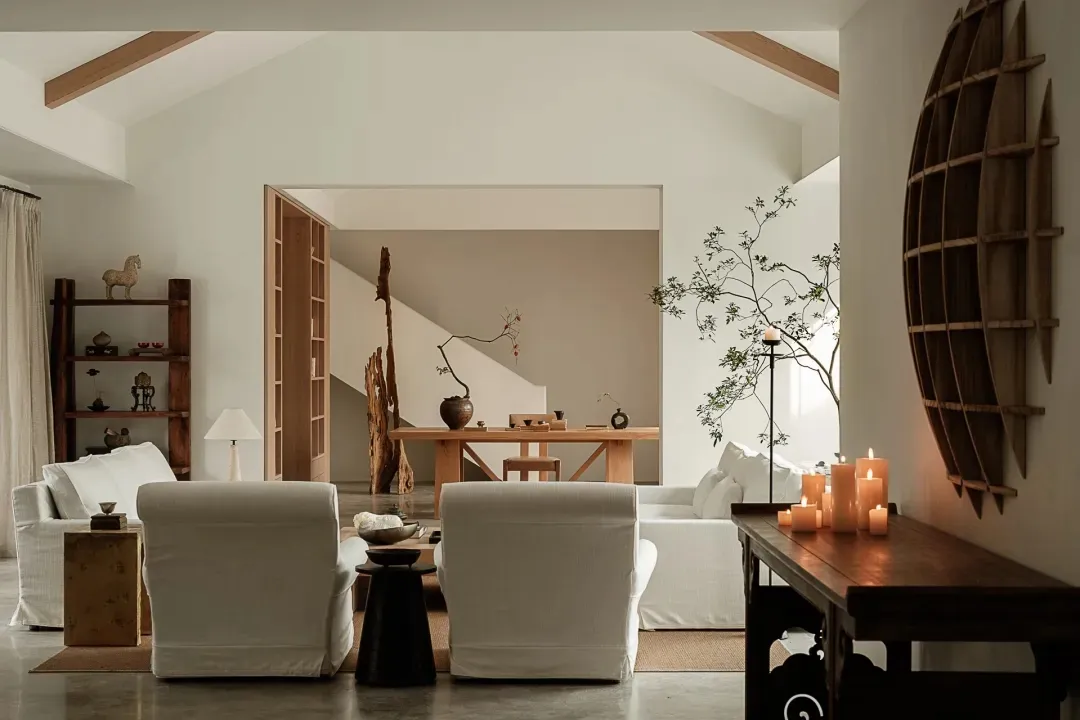 A living room with white and wooden furniture. Multiple seating options, a low coffee table, and a side table adorned with ca