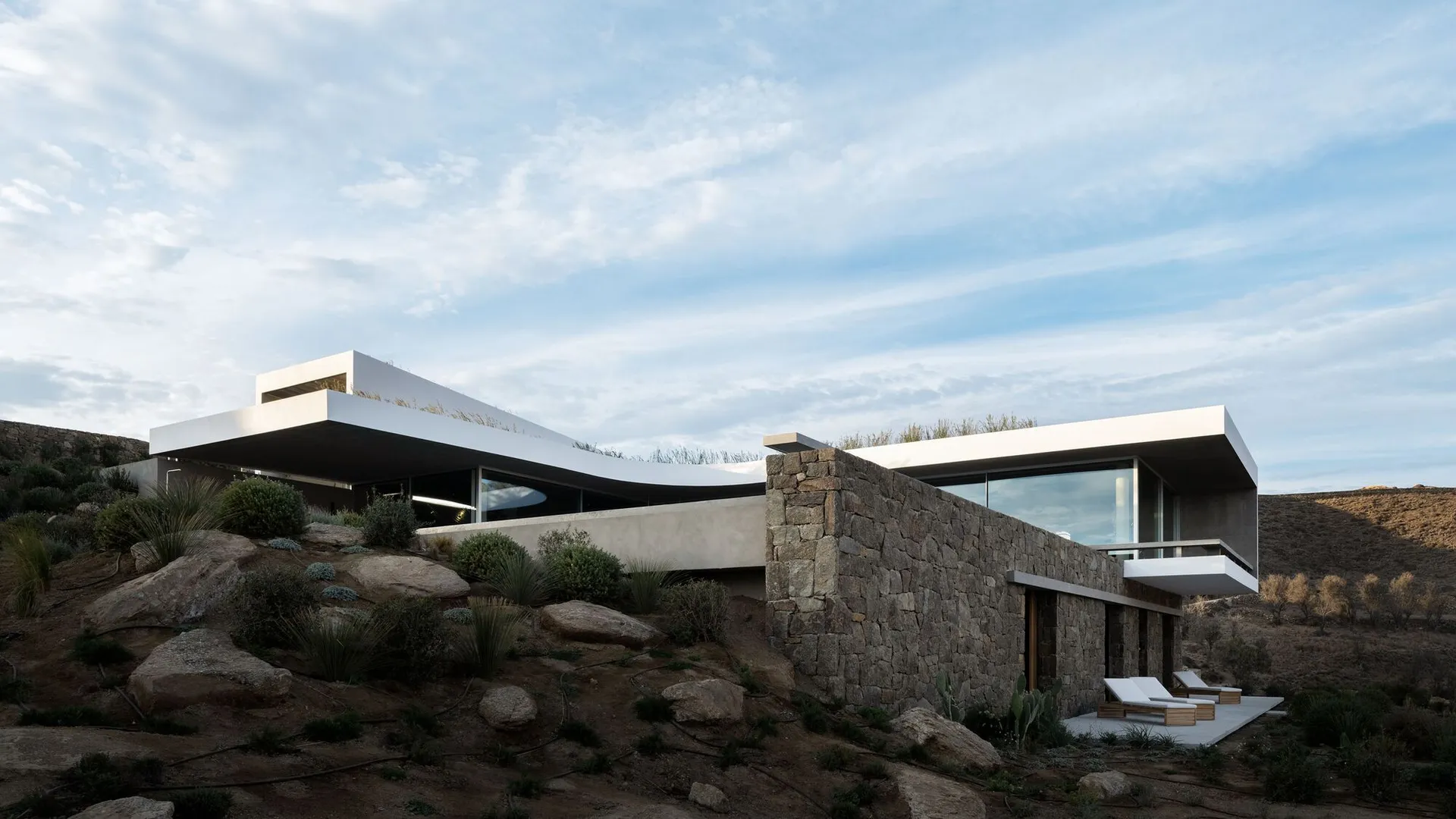 A modern house with a concrete structure and large windows overlooking the landscape.
