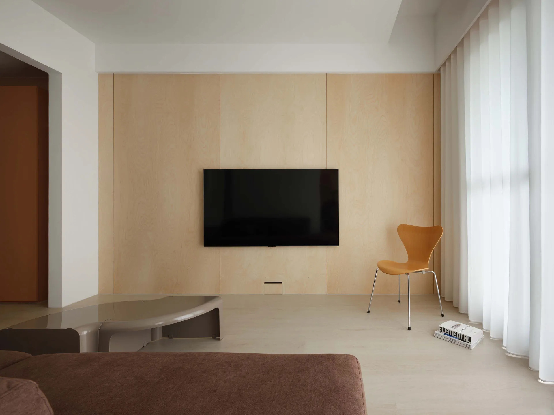 A minimalist living room with wooden walls, a glass coffee table, and an orange chair.