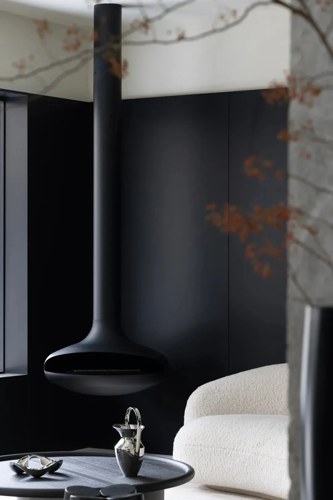 A minimalist living room with a black steel fireplace and white armchair, featuring sleek and modern design elements.