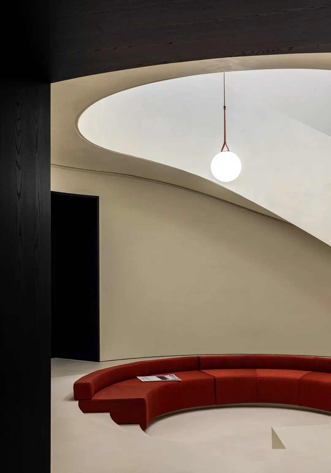 A modern lobby with a curved concrete seating area and a spherical light fixture hanging from the ceiling.