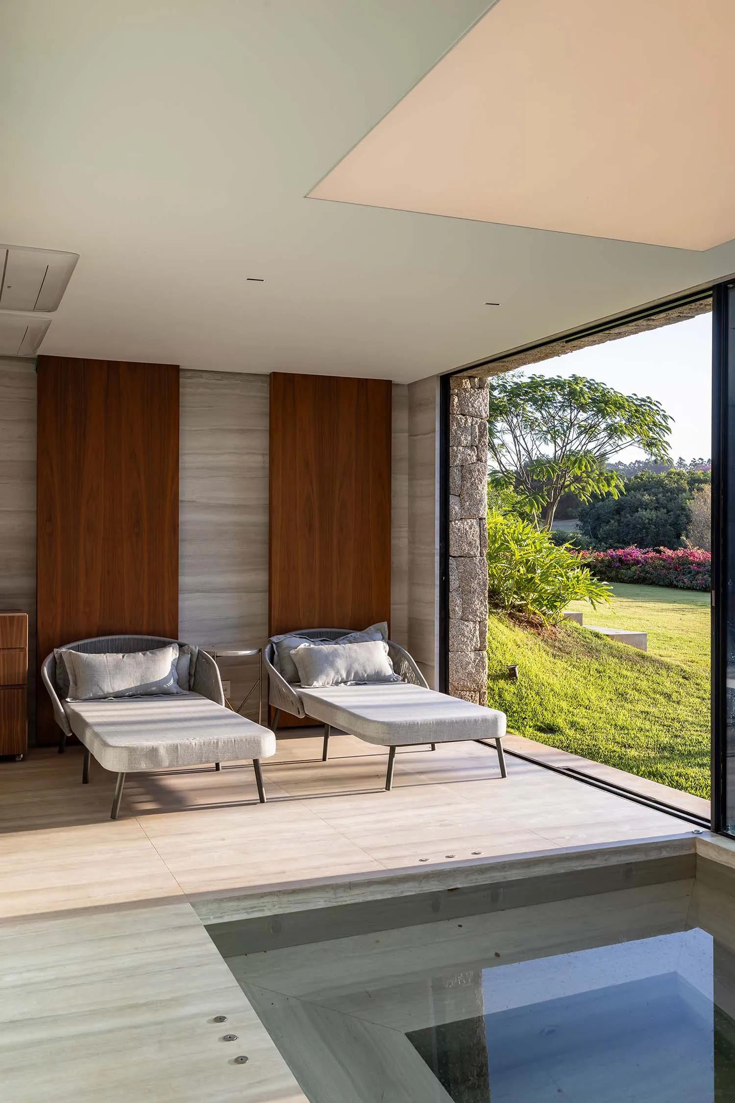 Contemporary living room featuring modern furniture, wooden walls, stone accents, and large glass windows overlooking a lush