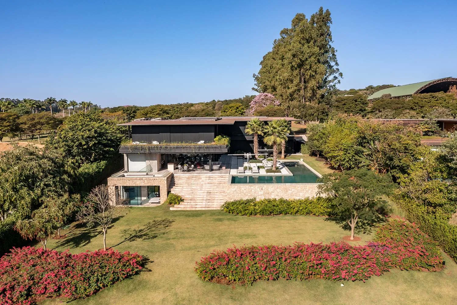 A modern residential home with a stone exterior, glass walls, and a large pool surrounded by greenery.