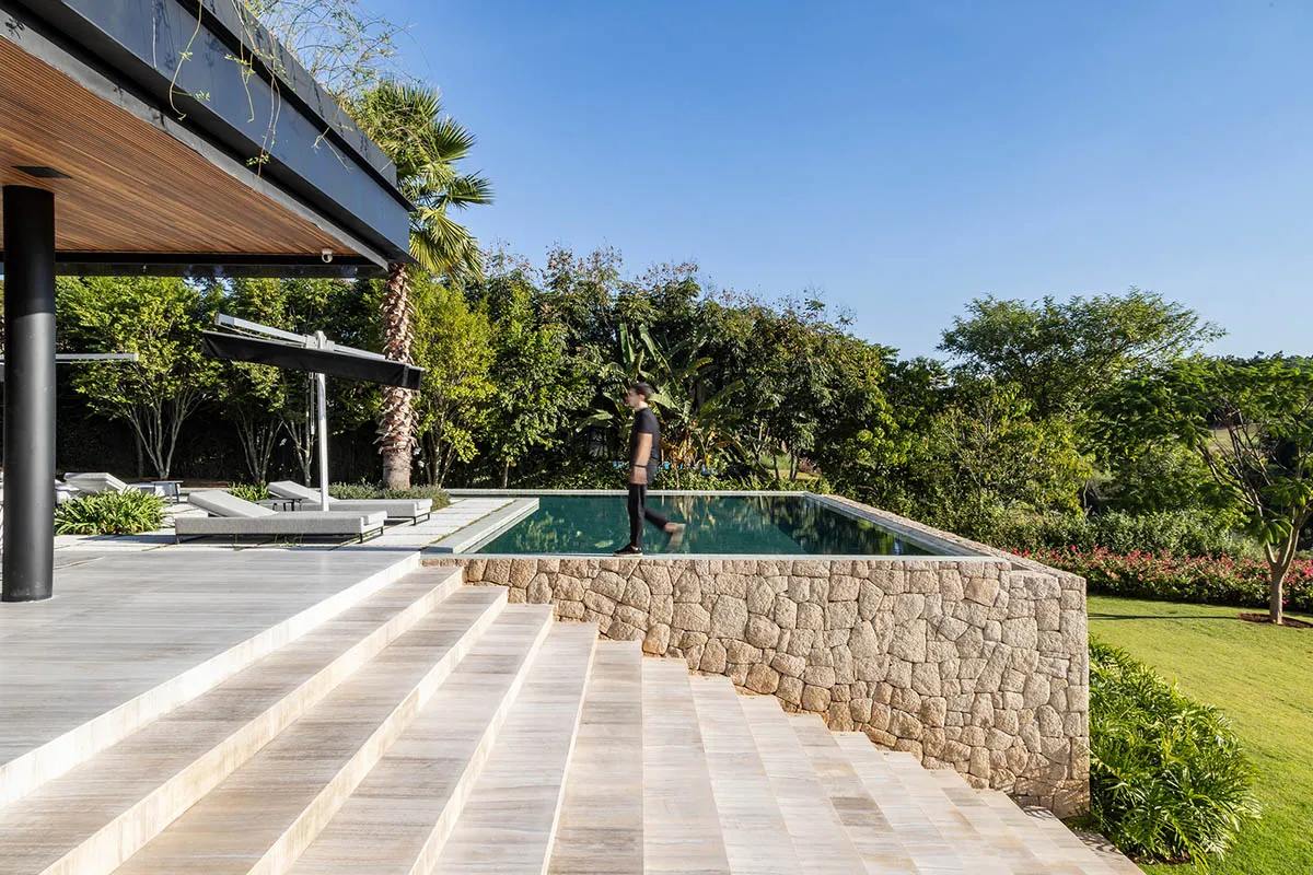 A modern residential area featuring a stone-edged pool with a covered patio and lush green surroundings.