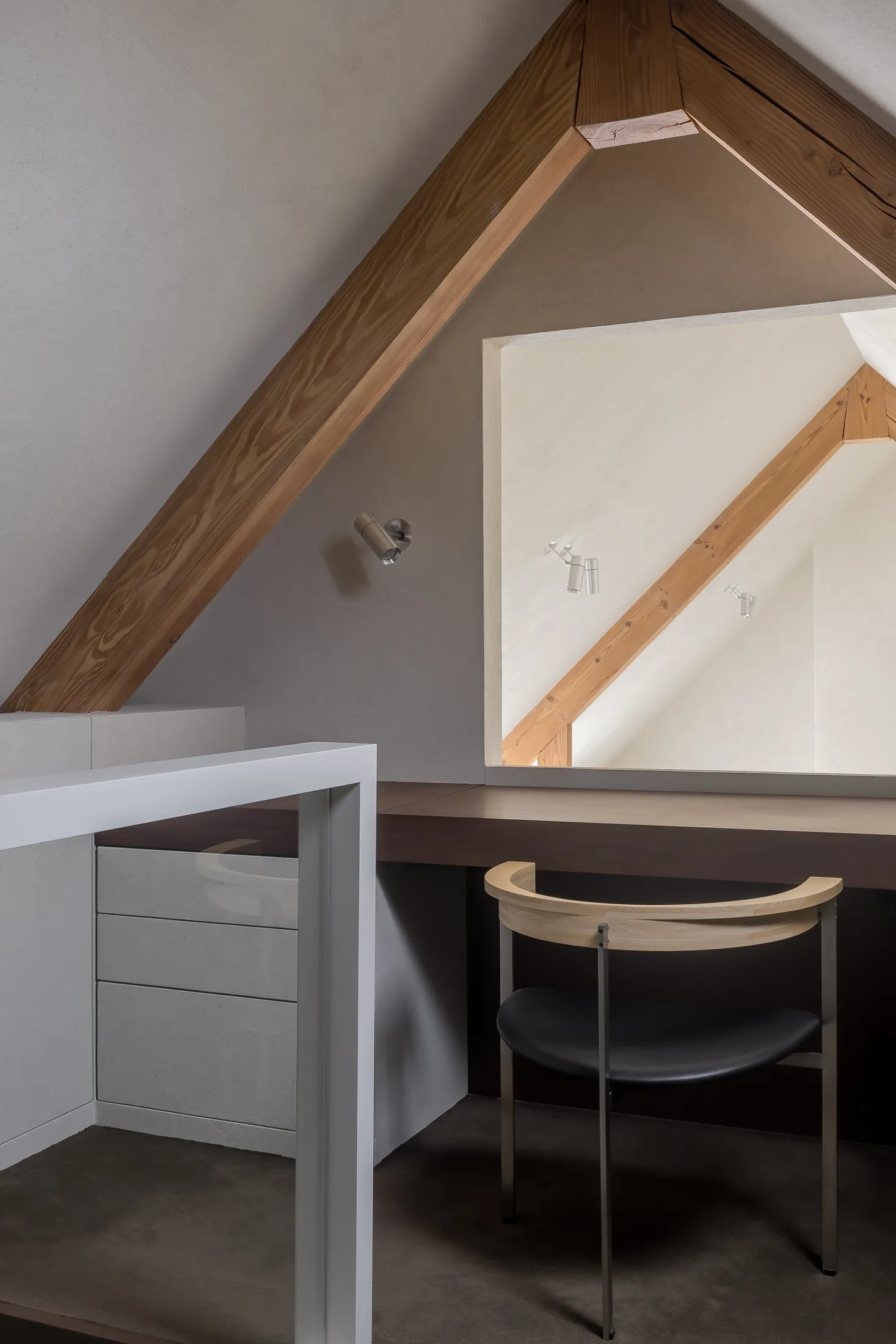 A modern home office features a concrete floor, wooden beams, and a metal desk.
