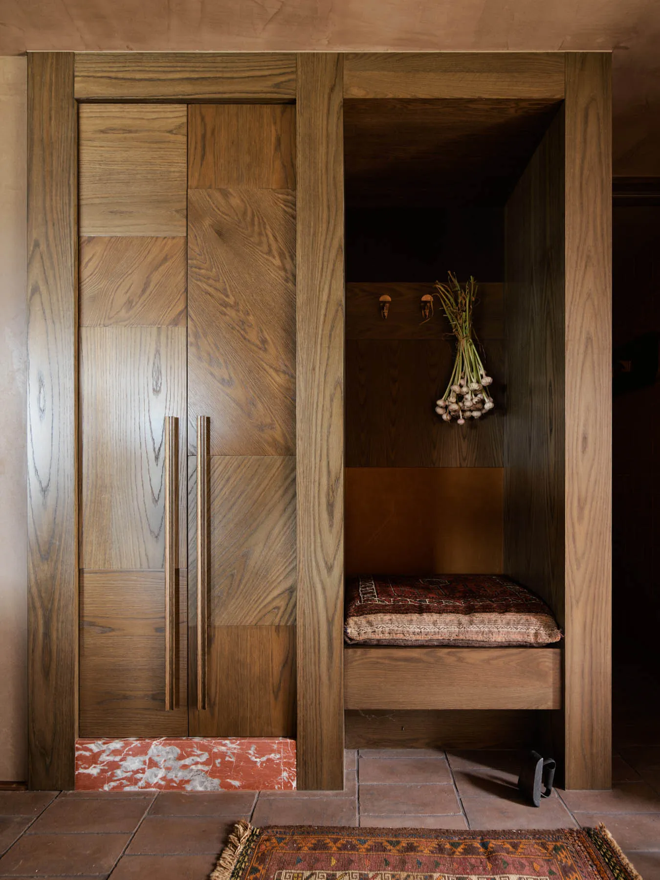 A modern wardrobe or storage nook made of oak wood, featuring a cushioned seating area and decorative onion bunch.