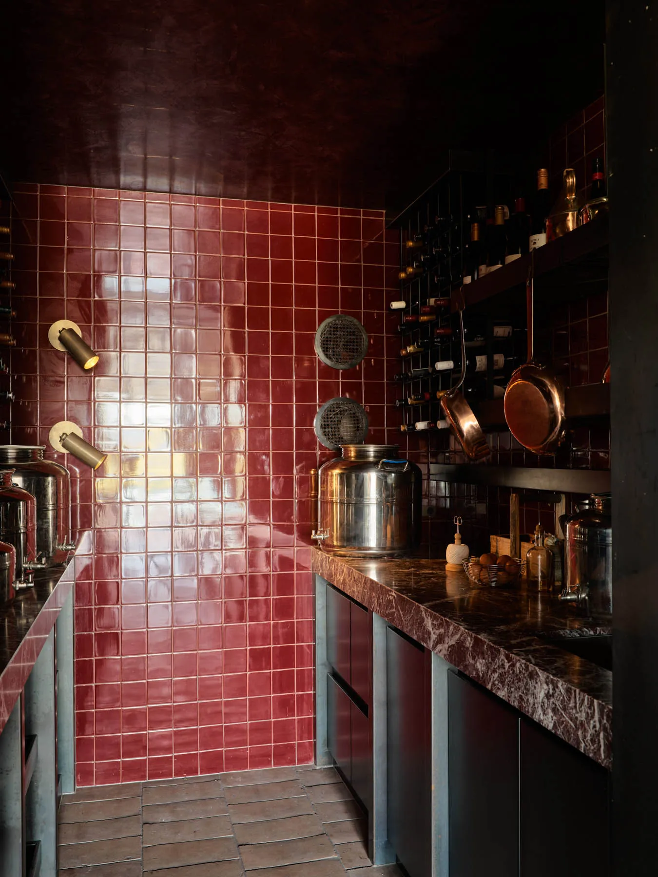 An industrial-style kitchen with red tile walls, metallic appliances, and various cooking utensils.