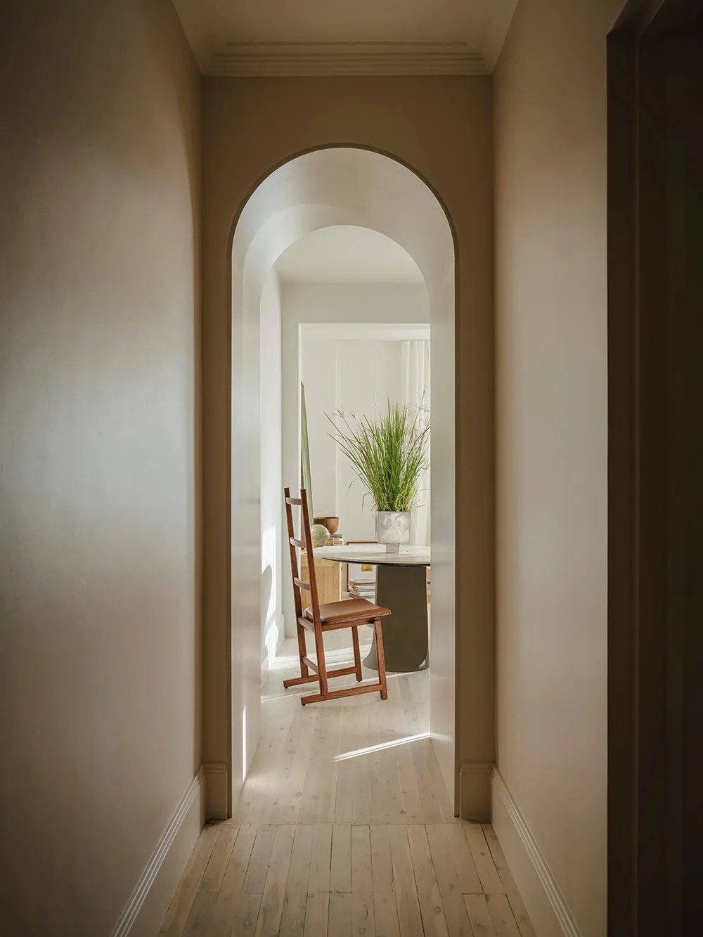 A minimalist corridor with an architectural arch, featuring wooden elements and plants.