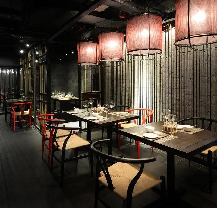 An industrial-style restaurant interior with wooden seating, fabric lighting fixtures, and metal elements.