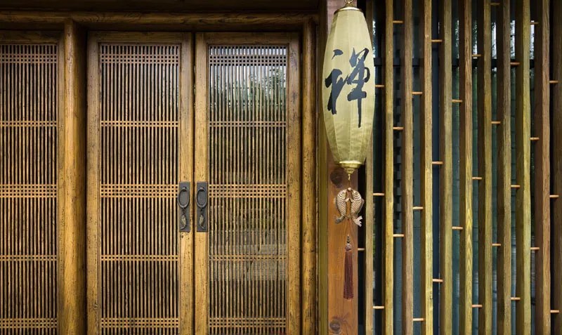 A minimalist wooden door with a traditional Japanese lantern hanging on the side, featuring Chinese characters for 'zen' and