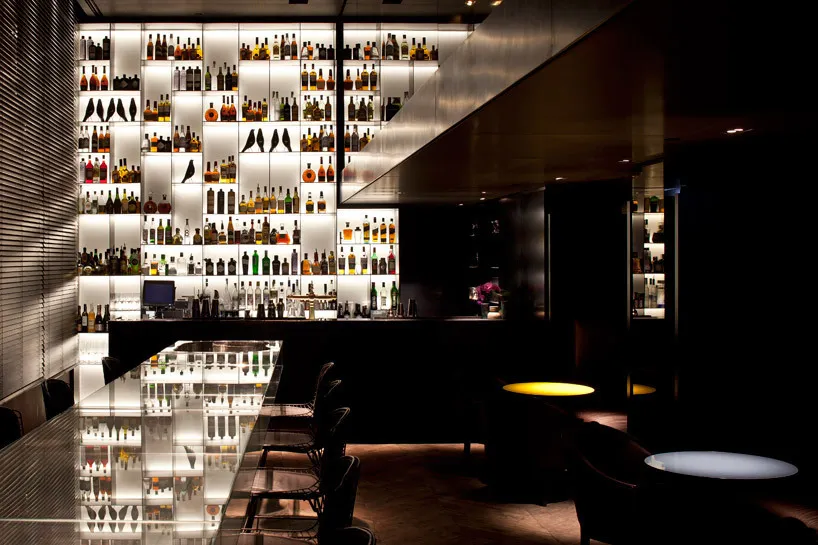 A modern bar with backlit metallic shelves displaying a variety of bottles and a sleek, contemporary design.