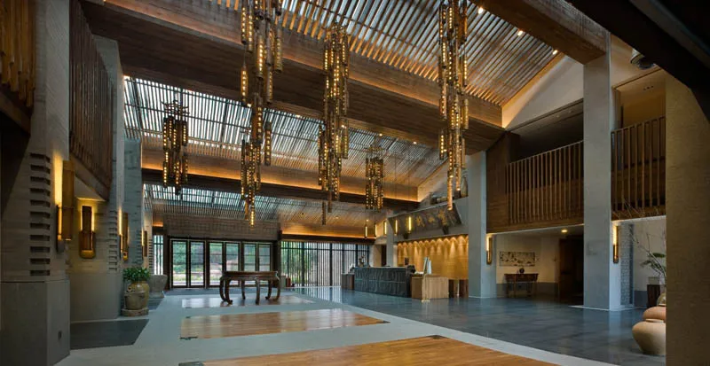 Modern hotel lobby with wooden flooring and ceiling, large windows, and hanging chandeliers.