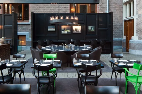 A modern restaurant interior featuring black metallic furniture adorned with green accents, including green chairs and green
