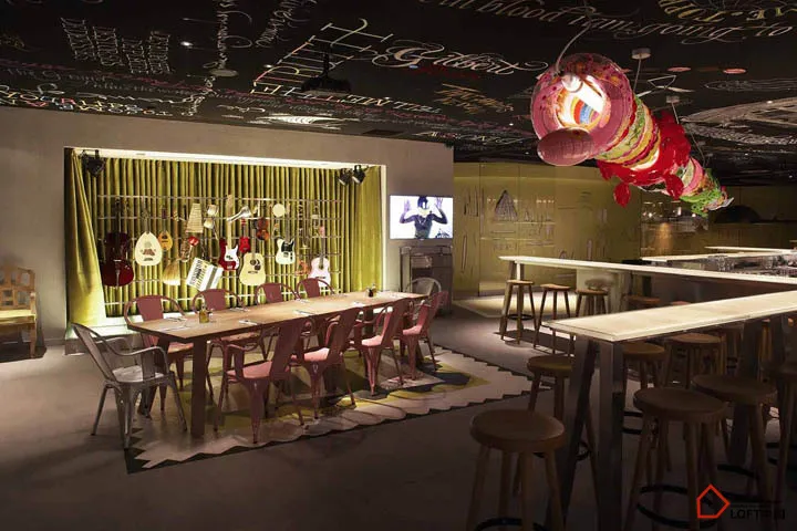 Industrial-style restaurant and bar interior with metal tables, wooden chairs, and glass chandeliers.