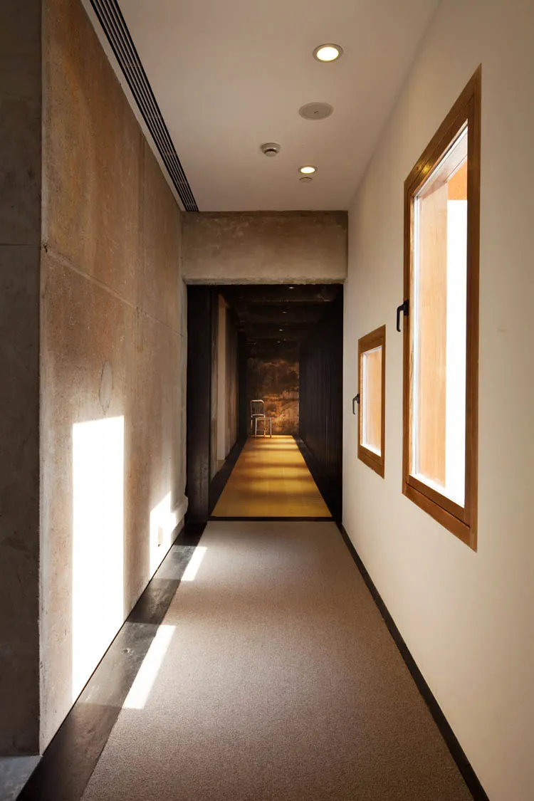 A modern minimalist interior with a concrete wall, a hallway, and a window letting in natural light.