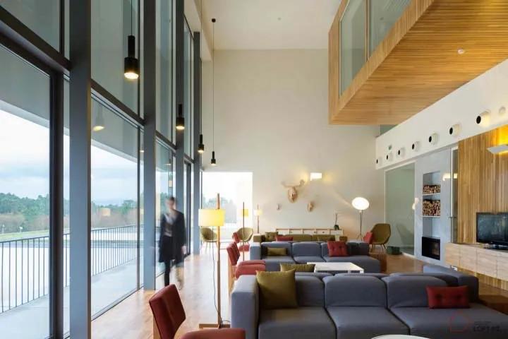 Modern living room with large windows, wooden ceiling, and a mix of fabrics and wood.