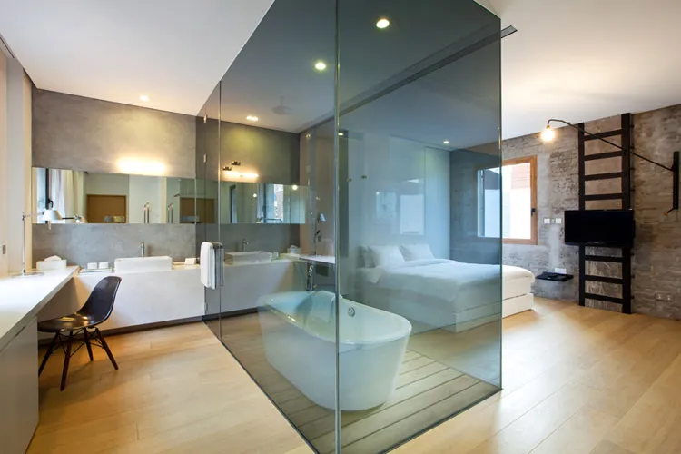 A modern minimalist bedroom featuring a glass-enclosed bathtub and a concrete wall.