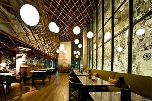 A spacious modern restaurant with industrial design elements including wooden beams, concrete walls, and large glass windows.