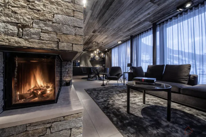 Modern lounge area with a concrete fireplace, dark furniture, and large windows.