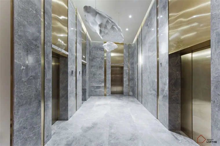 A modern office corridor with marble walls and floors and hanging art installations.