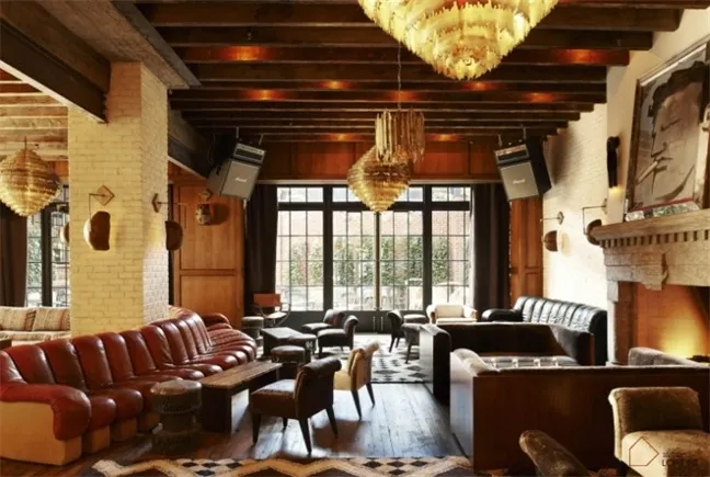 A cozy, industrial-themed hotel lounge featuring brick walls, wooden accents, leather furniture, and metallic chandeliers.