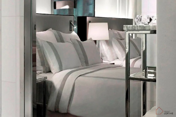 A minimalist bedroom with white-on-white striped bedding and a sleek, modern headboard and bedside table.