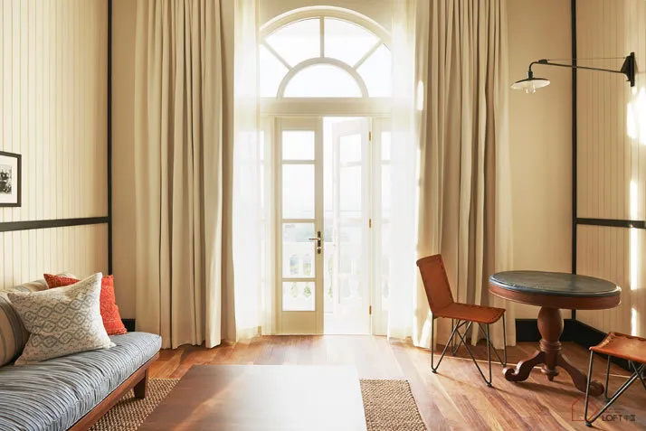 A modern minimalist living room featuring a grey couch with orange and white pillows, a wooden coffee table, and hardwood flo